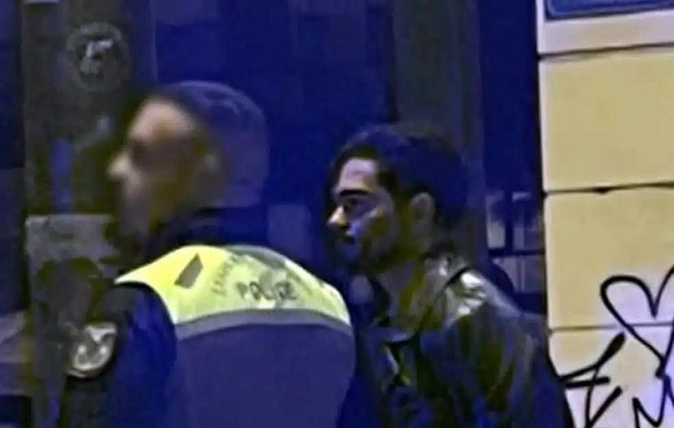 Ο Χρήστος Μάστορας με χειροπέδες, ενώ έχει δίπλα του έναν αστυνομικό. 